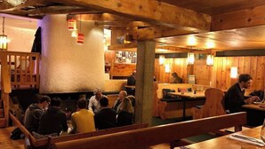 A cozy restaurant with wooden interiors, a central pillar, and patrons seated at tables. - Hôtel les Lorès (Val-d'Isere)