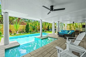 Ein überdachter Außenbereich mit Pool, weißen Liegestühlen und Deckenventilator.