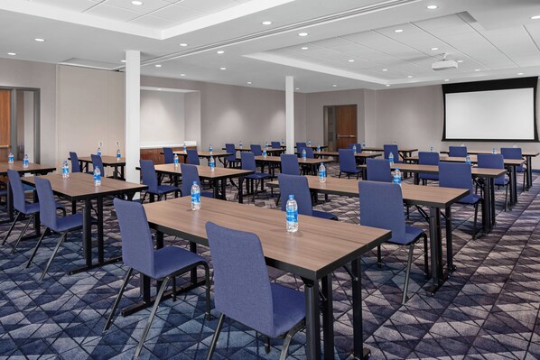 A conference room with multiple tables, chairs, and a projector screen. - Courtyard by Marriott Lansing Downtown (Lansing)