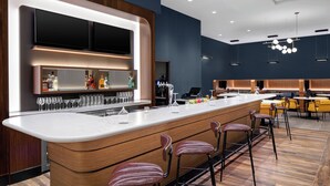 A modern bar area with a long counter, bar stools, and a television screen above. - Courtyard by Marriott Lansing Downtown (Lansing)