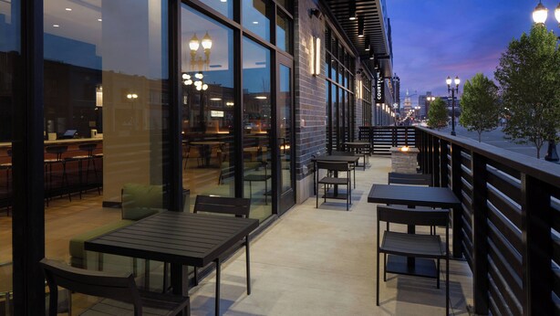 An outdoor seating area with tables and chairs, a railing, and a view of the cityscape. - Courtyard by Marriott Lansing Downtown (Lansing)