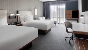 A hotel room with two beds, a desk, a chair, a TV, and a large window with curtains. - Courtyard by Marriott Lansing Downtown (Lansing)