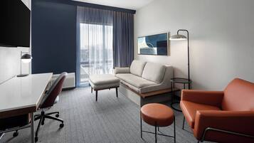 A hotel room with a sofa, armchair, ottoman, desk, and a flat-screen TV.