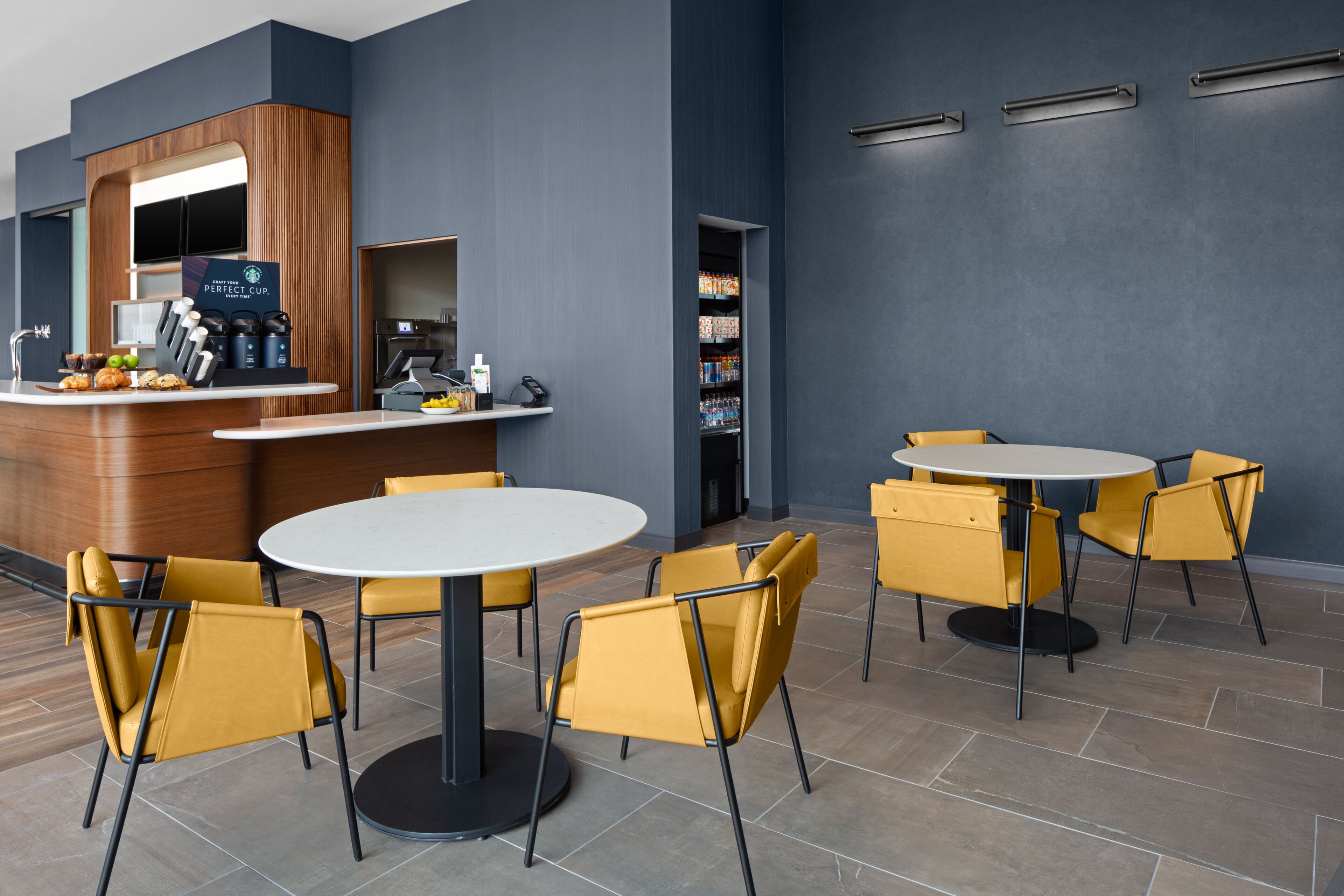 Un hall d’hôtel moderne comprenant un comptoir d’accueil, un espace salon et un coin café.