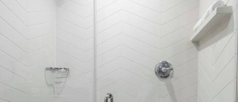 A modern shower with a glass door, a chrome showerhead, and a built-in towel rack.