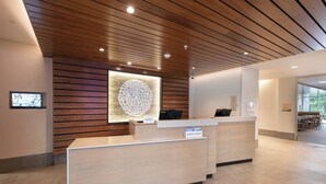 Un comptoir d’accueil d’hôtel au design moderne, un grand élément décoratif mural et un espace salon visible au fond.