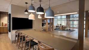 Un espace bar moderne avec des tabourets en bois, des luminaires suspendus et un grand téléviseur à écran plat.