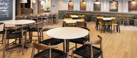 A restaurant with round tables and chairs, a green booth area, and wall-mounted pendant lights.