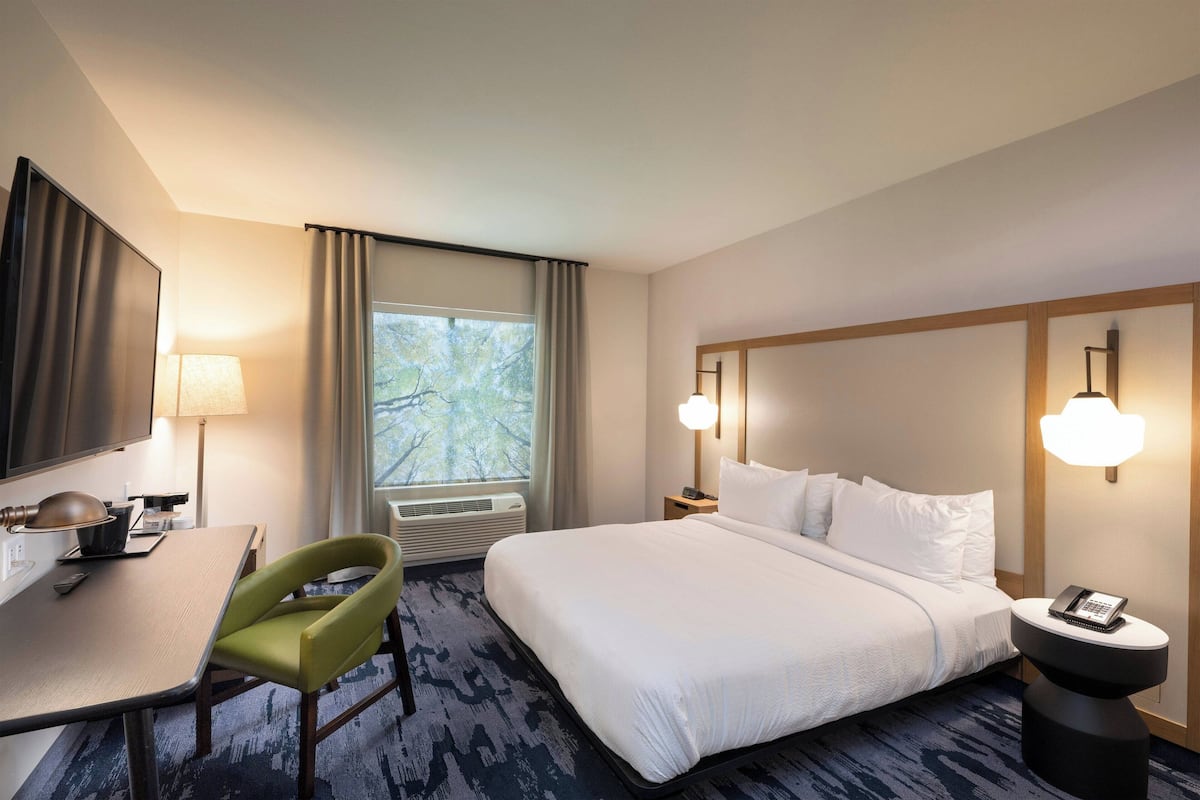 Habitación de hotel con cama, escritorio, silla, lámpara y ventana con cortinas.