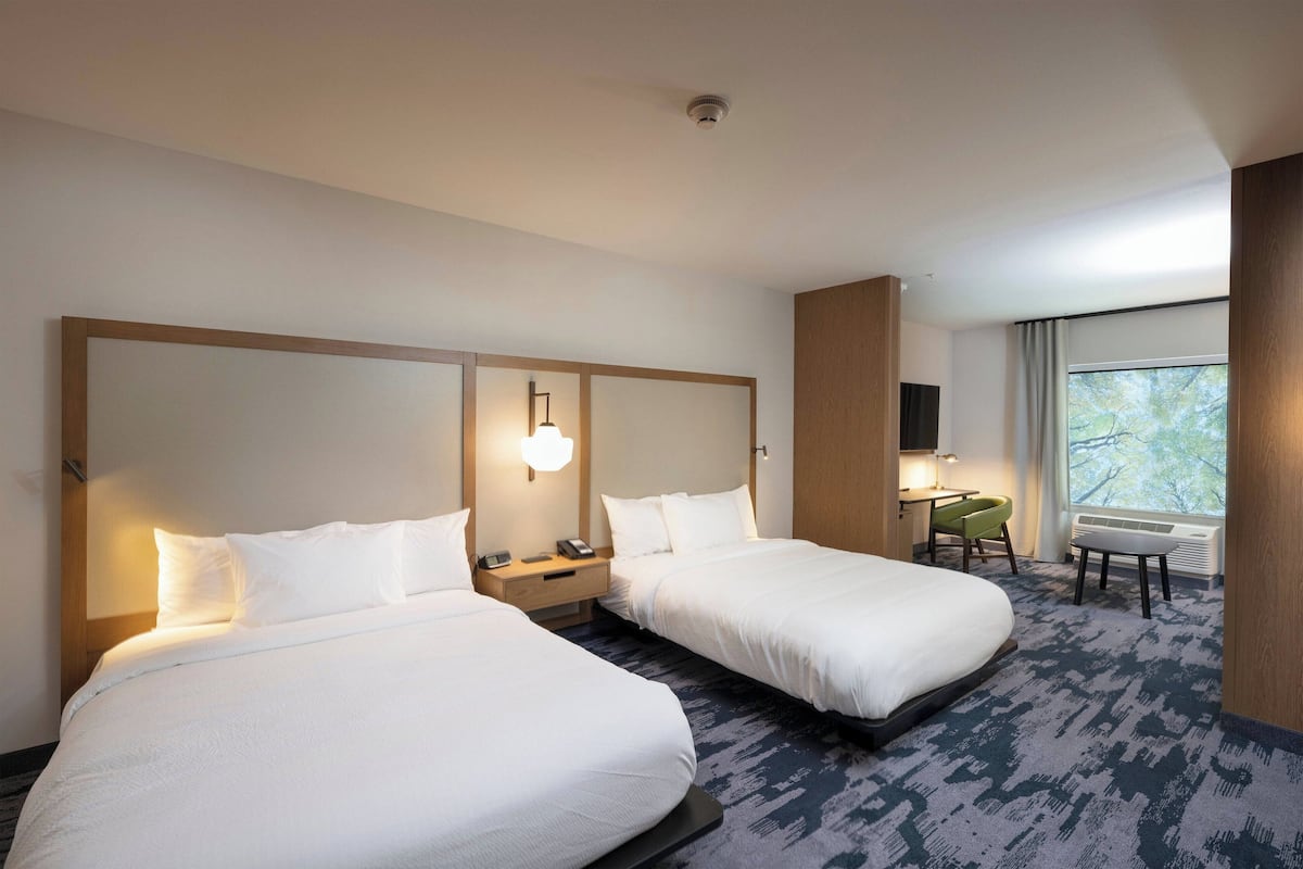 Habitación de hotel con dos camas, un escritorio, una silla y una ventana con vistas.
