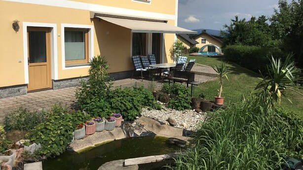 A yellow building with a patio, outdoor seating, and a small pond. - Haus Ruhland (Tiefenbach)