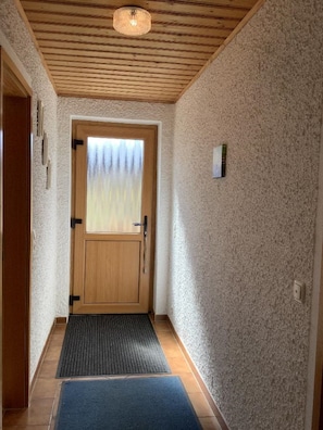 A hallway with a wooden door, a window with frosted glass, a textured wall, and a small light switch. - Haus Ruhland (Tiefenbach)
