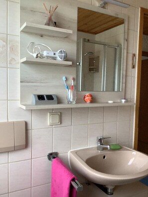 A bathroom with a sink, mirror, and shelves with toiletries. - Haus Ruhland (Tiefenbach)