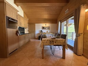 A wooden interior with a kitchen and dining area, featuring a table set for dining and a view through the glass door.