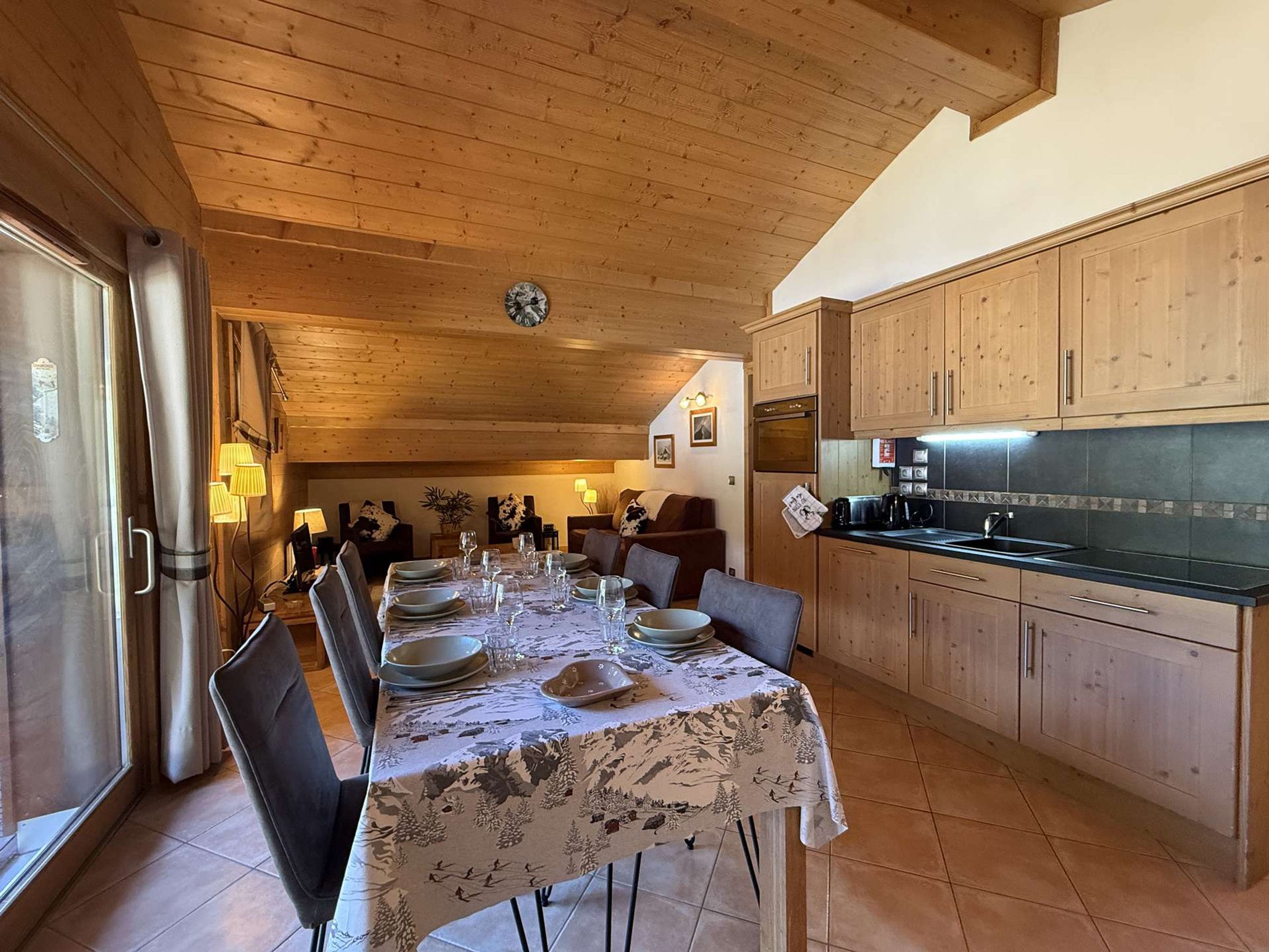 Un comedor con una mesa dispuesta para cuatro personas, armarios de madera y una cocina con encimera negra.
