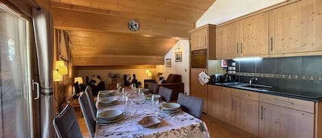 Un coin repas avec une table dressée pour quatre personnes, des meubles en bois et un espace cuisine doté d’un comptoir noir.