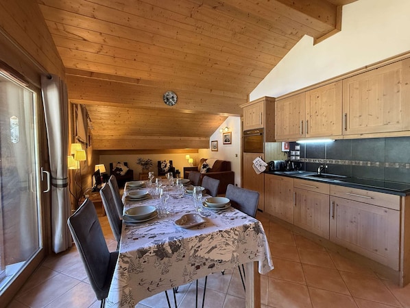 A dining area with a table set for four, wooden cabinets, and a kitchen area with a black countertop.