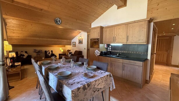Un coin repas avec une table dressée pour quatre personnes, des meubles en bois et une cuisine dotée d’un plan de travail noir.