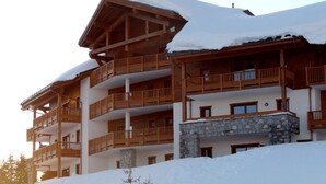 Un bâtiment en bois à plusieurs étages, doté de balcons et d’une base en pierre, entouré de neige.