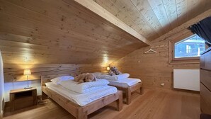 Une chambre dans un chalet en bois, avec deux lits, une table de chevet, une lampe et une fenêtre.