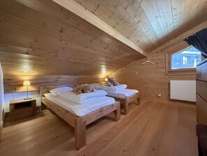 Camera da letto in una baita di legno, con due letti, un comodino, una lampada e una finestra.