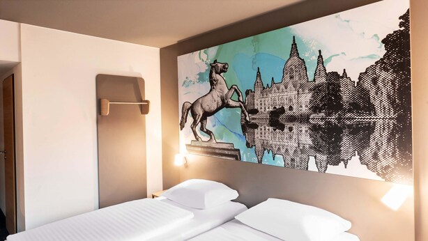 A hotel room with a bed, a nightstand, and a wall-mounted artwork depicting a horse and cityscape.