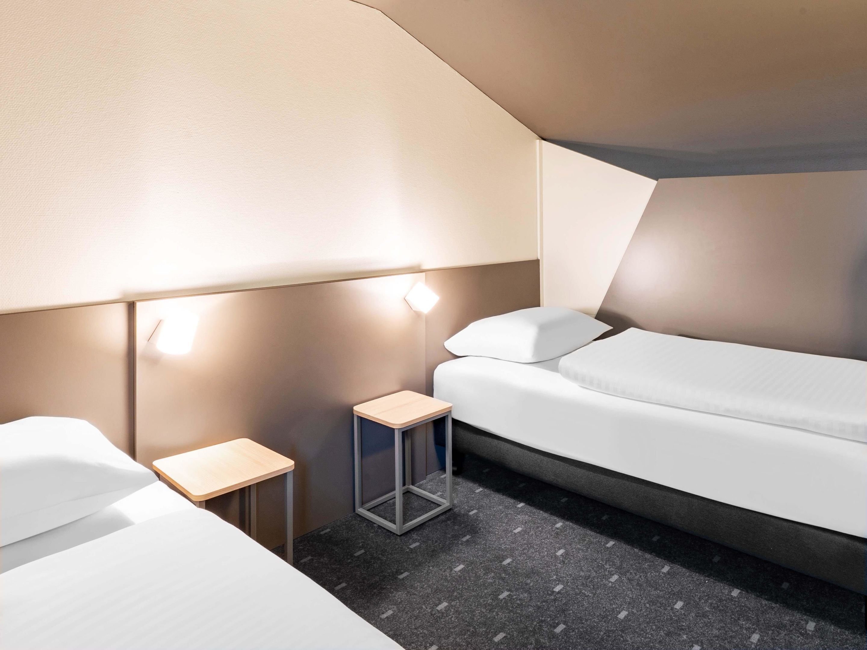 A modern hotel room with a bed, a small bedside table, and a lamp.