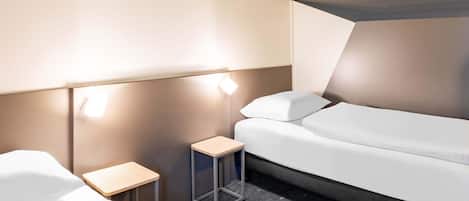 A modern hotel room with a bed, a small bedside table, and a lamp.
