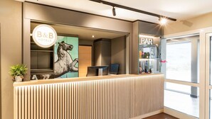 Un comptoir d’accueil orné du logo de B&B Hotels, un espace bar et une grande fenêtre offrant une vue panoramique.