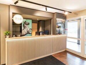 Een receptiebalie met een logo voor B&B Hotels, een bar en een groot raam met uitzicht.