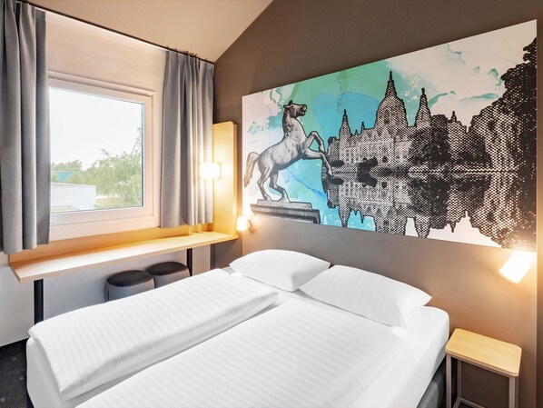 A hotel room with a bed, a window with curtains, a wall-mounted lamp, and a large cityscape painting. - B&B Hotel Hannover-Nord (Hannover)