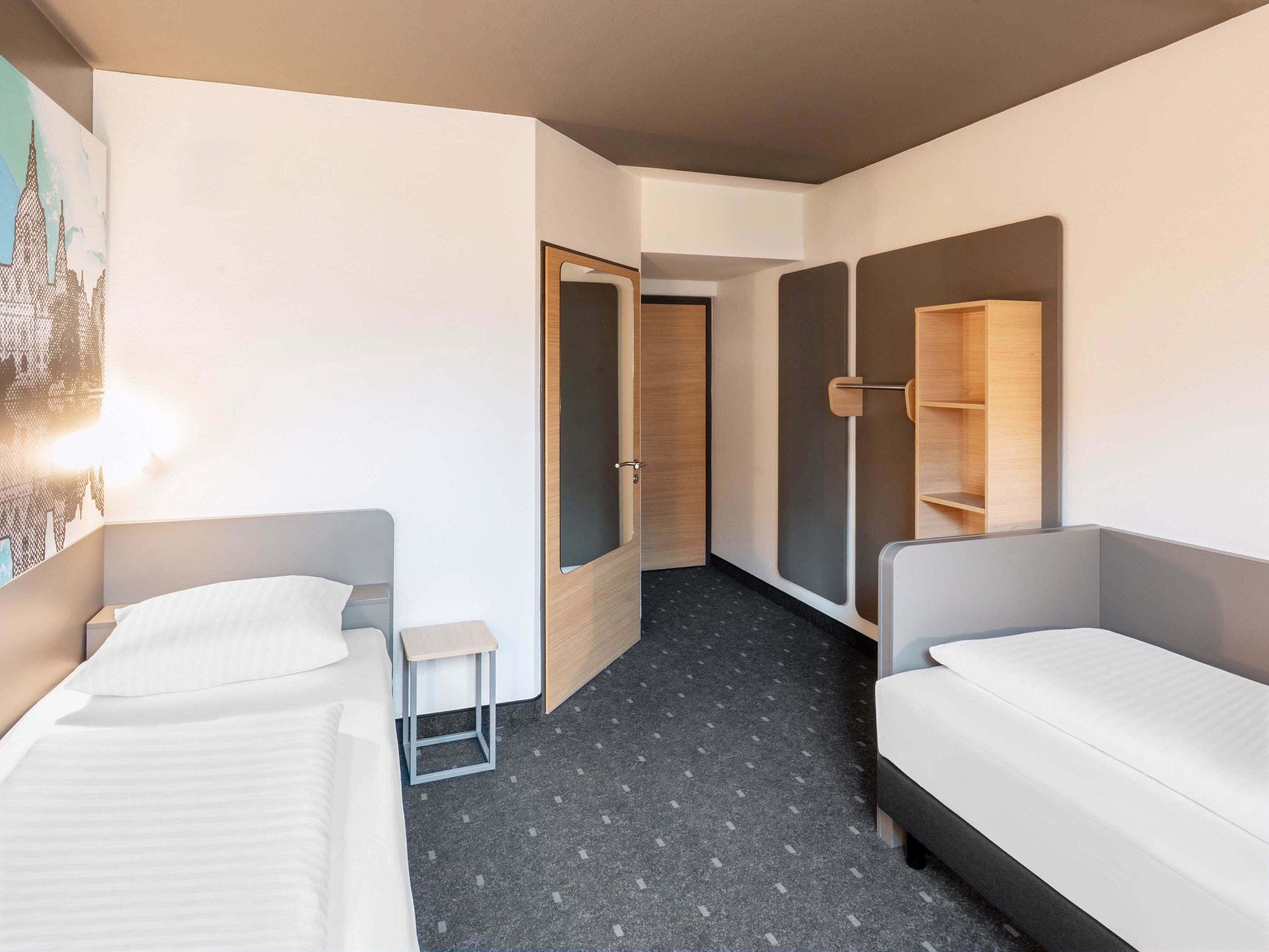 A hotel room with two single beds, a small table, a mirror, and a wardrobe.