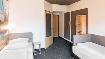 Habitación de hotel con dos camas individuales, una mesita, un espejo y un armario.