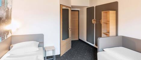 A hotel room with two single beds, a small table, a mirror, and a wardrobe.