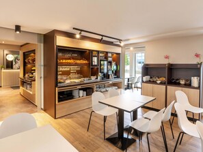 Een modern café met een toonbank waarop eten en drinken staan, witte stoelen rond een tafel, en uitzicht op het buitengebeuren.