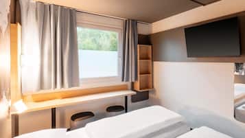 Un dormitorio compacto con una cama individual, una ventana con cortinas, un televisor montado y un estante pequeño.