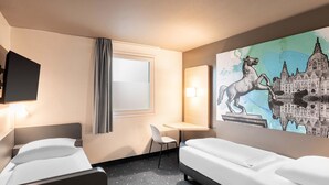 Une chambre d’hôtel équipée d’un lit, d’un bureau, d’une chaise, d’une télévision et d’une grande œuvre d’art murale.