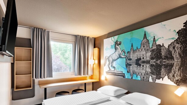 Une chambre d’hôtel avec un lit, un bureau, une chaise, une étagère et une grande fenêtre avec des rideaux.