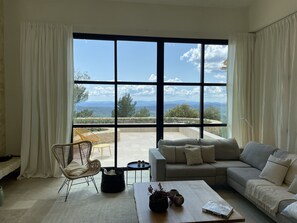Un salon spacieux doté d’une grande fenêtre offrant une vue sur les montagnes et les arbres au loin.