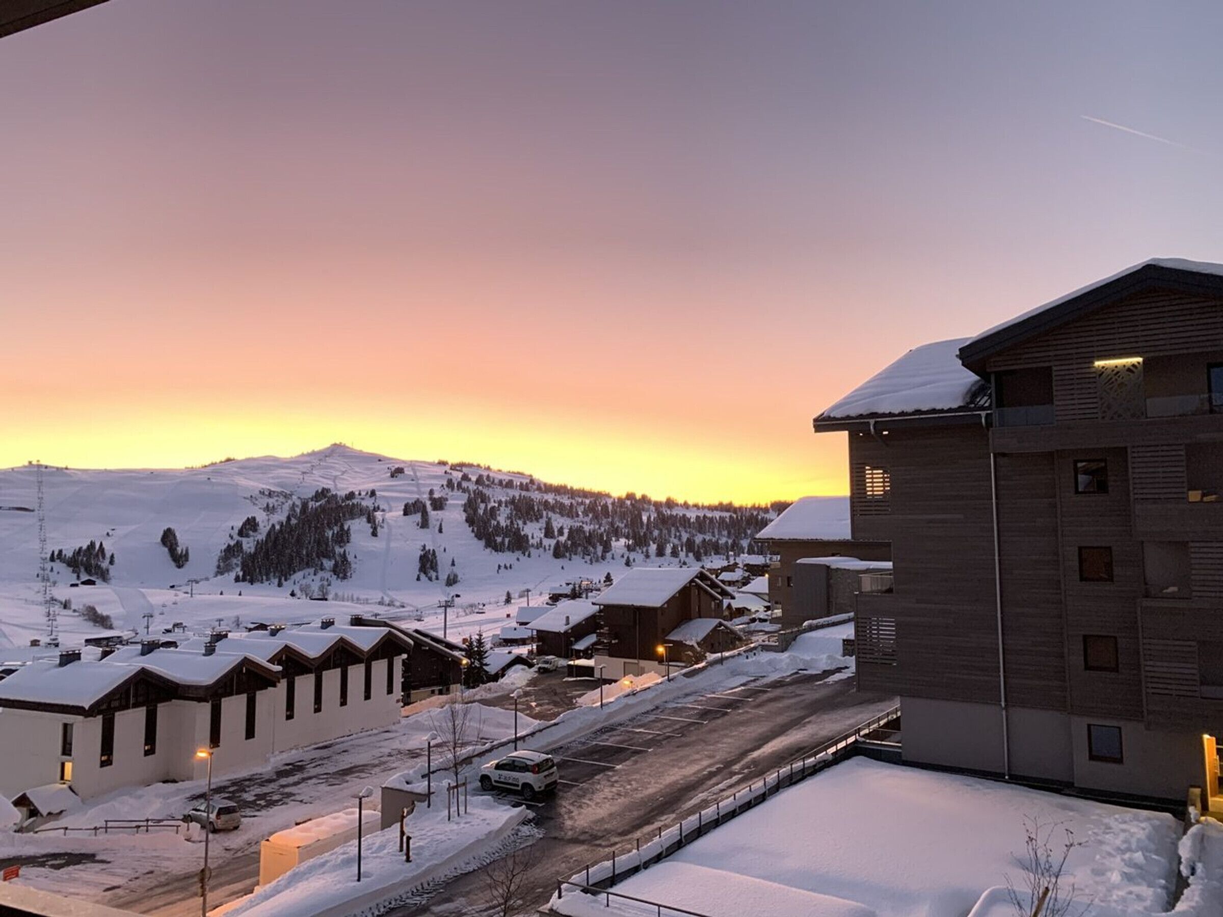 Schneebedeckte Landschaft mit Gebäuden und einem Berg im Hintergrund bei Sonnenuntergang.