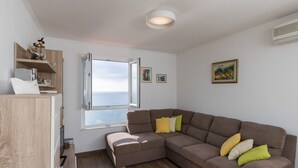 Ein modernes Wohnzimmer mit Ecksofa, Holzschrank, Fenster mit Blick und einer Deckenleuchte.
