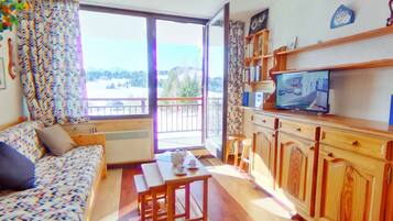 Un salon confortable avec un canapé, une table à manger et un téléviseur. Il y a un balcon avec vue sur l’extérieur.