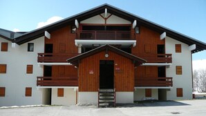 Ein zweistöckiges Gebäude mit Holzfassade, Balkonen und einem zentralen Eingang.