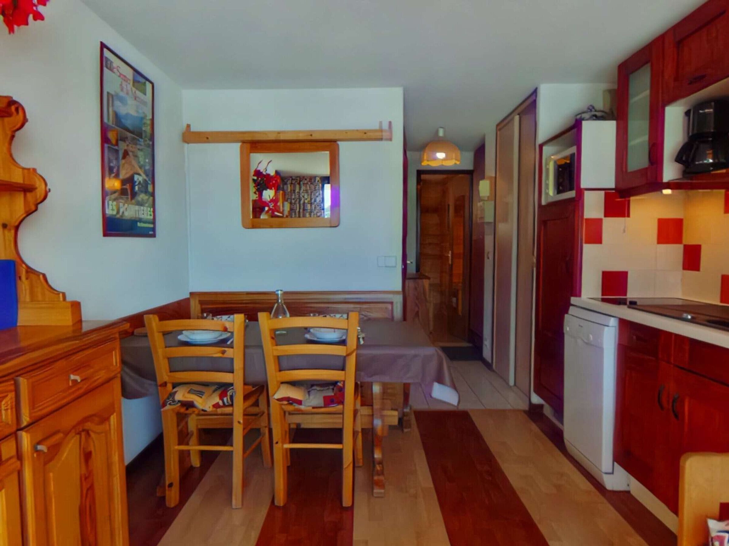 Une cuisine de taille réduite, dotée de meubles de rangement en bois, d’une table à manger avec des chaises et d’un petit réfrigérateur.