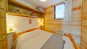 Ein gemütliches Holzblockhaus-Zimmer mit einem Bett, einem Nachttisch mit Lampe, einem Fenster mit Vorhängen und einem Regal mit Blumen.