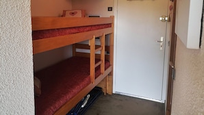Une chambre avec un lit superposé, une porte blanche et un petit placard au-dessus.