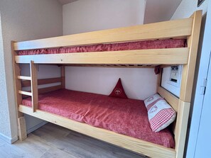 A bunk bed with a ladder on the left, a red mattress, and a pillow with a heart design.