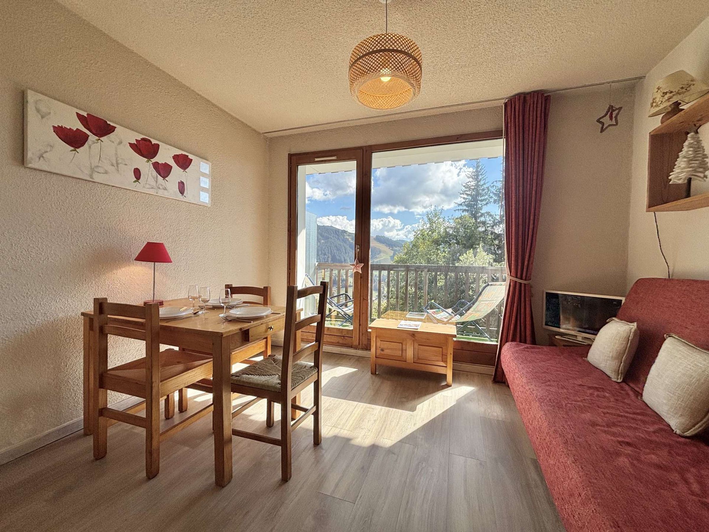 Un espace de vie chaleureux comprenant un coin repas, un canapé rouge et un balcon offrant une vue sur les montagnes.
