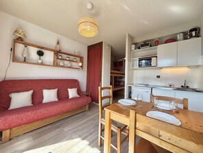 Un espace de vie compact comprenant un canapé rouge, une table à manger en bois et un coin cuisine.
