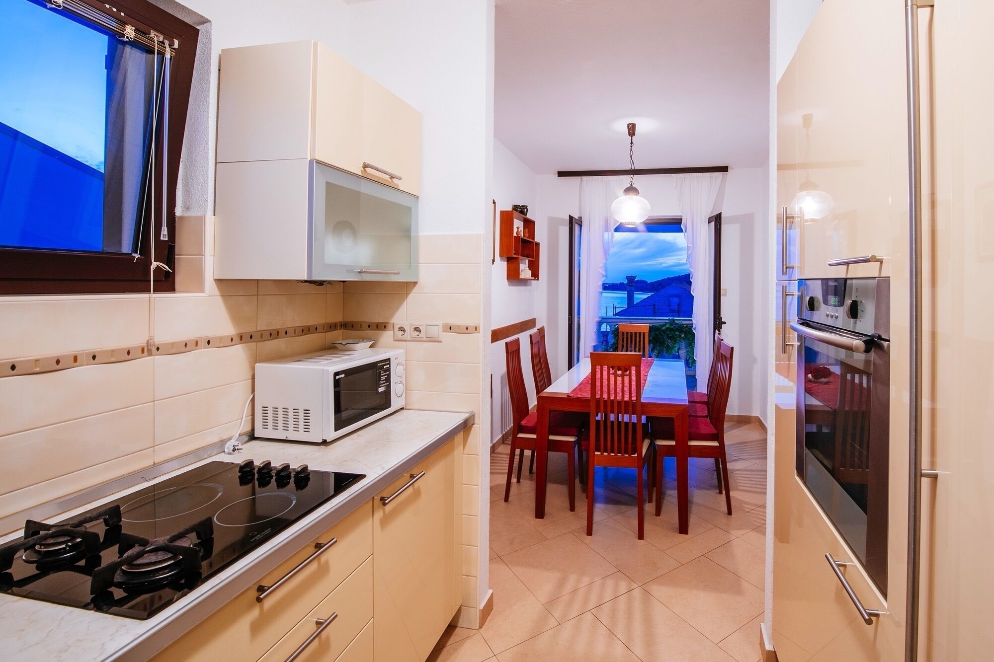 A compact kitchen with a gas stove, microwave, and oven. There is a dining area with a table and chairs, and a view of the outdoors through a window.